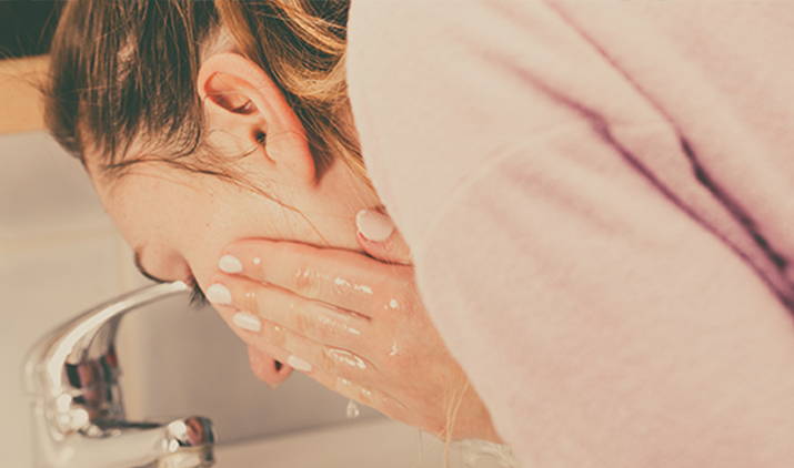 young woman rinsing her face at sink